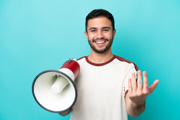 Wall Mural - Young Brazilian man isolated on blue background holding a megaphone and inviting to come with hand