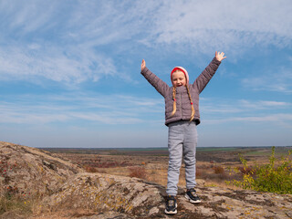 Adorable little traveler girl raising hands. Child climbing on mountain summit spending time on nature walking enjoying scenic landscape cloudy sky. Active lifestyle candid authentic family having fun