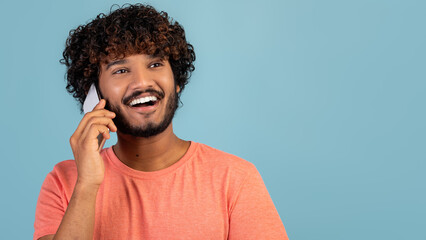 Wall Mural - Closeup of positive indian guy having phone conversation on blue