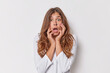 © WHstudio Leushin N - Omg concept. Speechless scared beautiful European woman with long hair keeps mouth opened stares bugged eyes reacts on shocking news keeps hands on face dressed casually isolated over white background