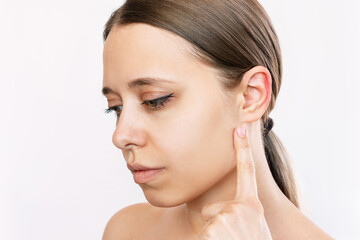 Wall Mural - Portait of a young caucasian woman pointing at her ear with her finger isolated on a white background. Correction of auricles, otoplasty