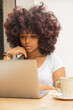 © Cavan Images - Young Afro woman in a coffee shop working online at her computer.