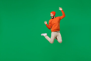 Wall Mural - Full size young exultant happy overjoyed excited fun cool man 20s in orange sweatshirt hat jump high clench fist celebrate isolated on plain green background studio portrait. People lifestyle concept.