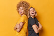 © wayhome.studio  - Positive two young pretty women stand back to each other keep arms folded laugh happily dressed in casual t shirts laugh at something funny isolated over yellow background. Friendship concept