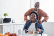 © LIGHTFIELD STUDIOS - happy and senior african american man standing behind wife during breakfast.