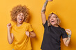 Studio shot of happy lively young women enjoy life shake arms feel energetic exclaim loudly wear casual basic t shirts isolated over yellow background have fun and dance. Happy emotions concept