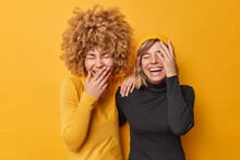 Photo Of Overjoyed Friendly Women Laugh Out Loudly Giggle As Hear Funny Joke Have Fun Chuckle At Camera Feel Positive Dressed In Casual Turtlenecks Isolated Over Yellow Background. Happiness Concept