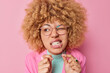 Dental health care concept. Beautiful young woman with curly bushy hair cleans teeth with dental floss wears transparent eyesglasses isolated over pink background shows how to floss correctly