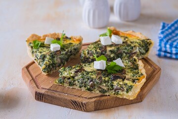 Canvas Print - Unsweetened sliced open pie, shortcrust pastry quiche stuffed with spinach, mushrooms and cheese on a wooden board on a light concrete background. Unsweetened pastry recipes.