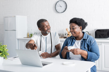 retired african american man pointing at laptop near wife.