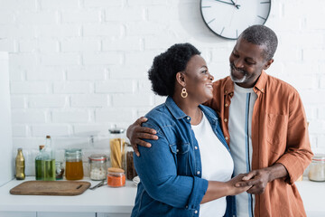 happy senior african american man looking at wife in kitchen.