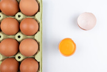Pack Of Brown Eggs With One Broken Open Egg With Raw Yolk And Shell On White Background.