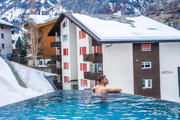 Wall Mural - Thoughtful man looking at snow covered houses while swimming in pool