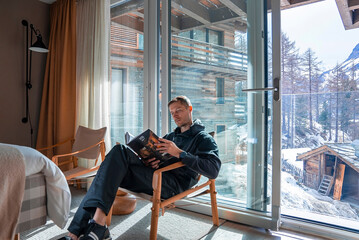 Wall Mural - Tourist reading journal while relaxing in bedroom at luxurious ski resort