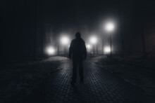 Sad Man Alone Walking Along The Alley In Night Foggy Park