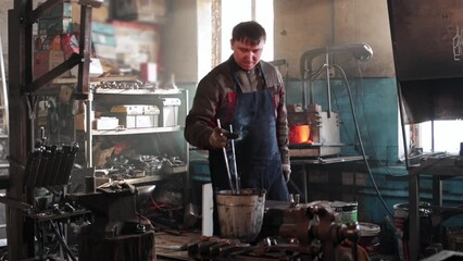 Wall Mural - Man blacksmith takes out heated metal detail out of the furnace and cooling down in a bucket of water