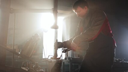 Wall Mural - Man blacksmith bending hot piece of metal using a form on an anvil and hitting the detail with a press