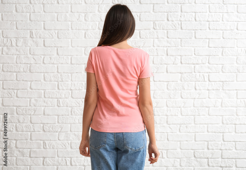 Young woman in blank t-shirt on white brick background, back view