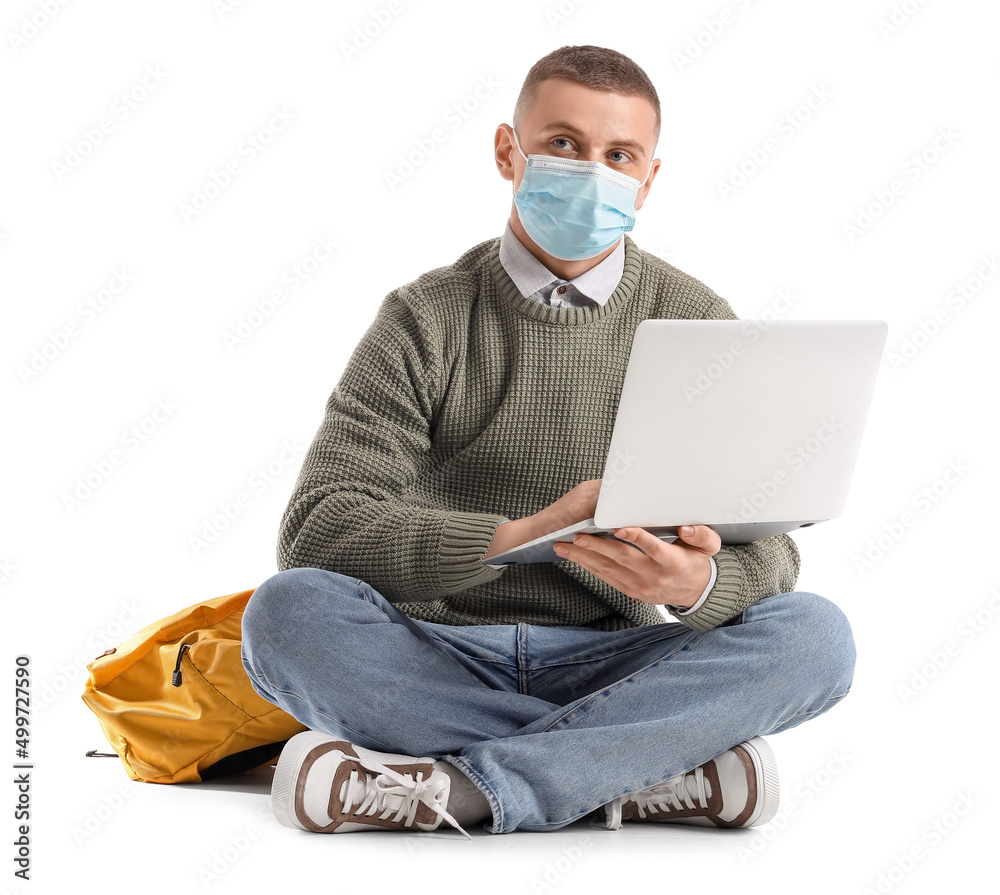 Male student in medical mask using laptop on white background