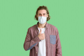 Poster - Young man wearing medical mask and showing thumb-up on green background