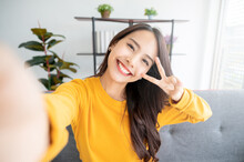 Pretty Young Asian Female With Big Smile Sitting At Living Room. She Having Fun Taking Light Cheerful Selfie On Blurred Background