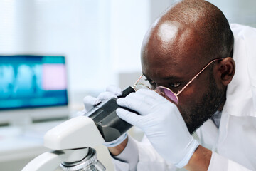 Aufkleber - Bald African American scientist in gloves and eyeglasses looking at new virus or bacteria in microscope while working in laboratory