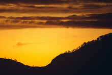 Silhouette Of A Mountain With Trees Against A Yellow Sunset
