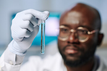 Aufkleber - Gloved hand of African American male researcher holding flask with light blue liquid and looking at it during scientific investigation