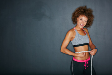 Wall Mural - Progress is impossible without change. Portrait of a sporty young woman measuring her waist against a grey background.