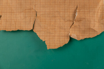 Ripped crumpled sheet of millimeter graph paper against a green background. Brown paper for drafting, design, engineering, and more. Abstract multitasking background.