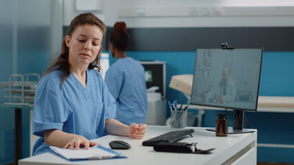 Wall Mural - Nurse using video call for conversation with doctor on computer. Medical assistant talking to medic on online video conference for remote advice and telemedicine while sitting in cabinet