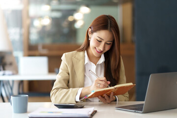 Wall Mural - Happy young Asian businesswoman is sitting smiling and taking notes happily in the office.