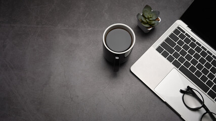 Fototapete - Top view laptop computer, coffee cup and eyeglasses on dark stone background. Copy space for your information content.