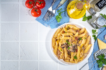 Italian mediterranean lunch concept. Penne pasta with creamy carbonara mushroom sauce. On a white tile table, with spices for dinner copy space