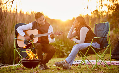 Poster - Life is better around the campfire. Shot of a you man playing his guitar to his wife outside while camping.