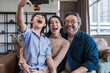 © saksit - Family smiling at camera. Happy family taking a selfie, smiling at a phone at home