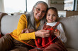 © Halfpoint - Little girl sitting on sofa with her grandmother and learning to knit indoors at home.