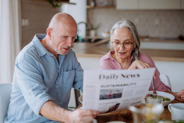 Wall Mural - Happy senior couple having breakfast and reading newspaper together at home.