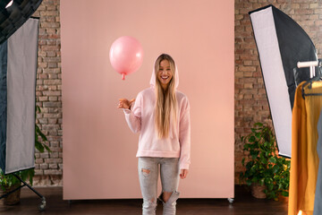 Wall Mural - Studio portrait of a happy young blonde woman with balloon over pink background.