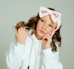 Wall Mural - teenage girl in a white hoodie in the studio on a white background various grimaces, she is young she has a mobile phone in her hands she takes a selfie and admires herself and a pink bandage.