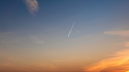 Wall Mural - Passenger plane flying in the blue sky at sunset, fast transport vapor trails