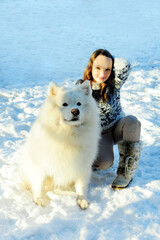 Wall Mural - teenage girl plays with a dog of the Samoyed breed dog fluffy snow-white and big she plays outside in the snow hugging and having fun girl beautiful and young she is brown-haired.