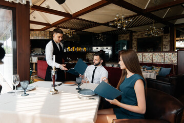 Wall Mural - A stylish waiter serves a young couple of a man and a woman who came on a date to a gourmet restaurant. Customer service in the restaurant and catering establishments.