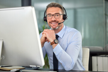 Im always ready for you. Portrait of a mature man wearing a headset while using his computer at work.