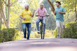 © G-images - Senior man riding bicycle with other old man and son running while having fun at park