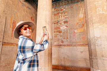 Travel blogger girl takes pictures on a smartphone at the famous Hatshepsut temple in the ancient city of Luxor in Egypt.