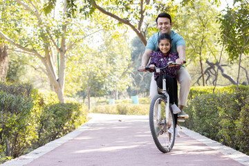 Wall Mural - Young man riding bicycle with daughter at park