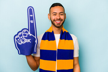 Wall Mural - Young sports hispanic fan man isolated on blue background happy, smiling and cheerful.