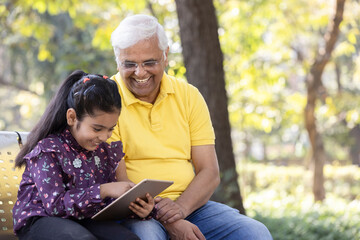 Wall Mural - Senior man with granddaughter having fun watching digital tablet at park