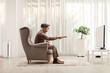 © Ljupco Smokovski - Elderly man in an armchair changing channels on TV with remote control in a living room